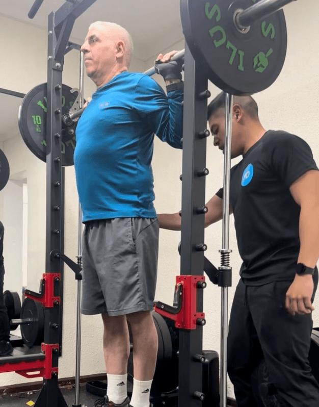 Entrenador de MD asistiendo a un paciente en sentadilla con barra